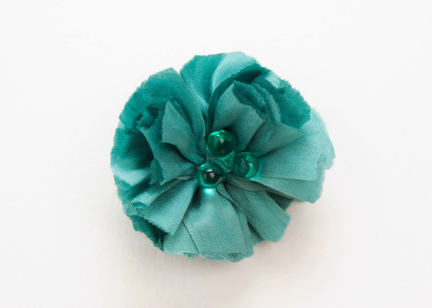 Front view of a teal silk flower charm with glass detail in center on a white background.