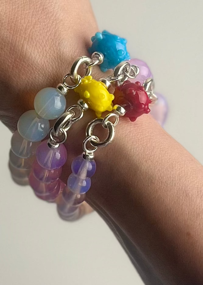 Wrist close up detail of three Opalite beaded bracelet stack with 3 lampwork glass urchin charms each in different colour.