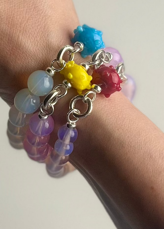 Wrist close up detail of three Opalite beaded bracelet stack with 3 lampwork glass urchin charms each in different colour.