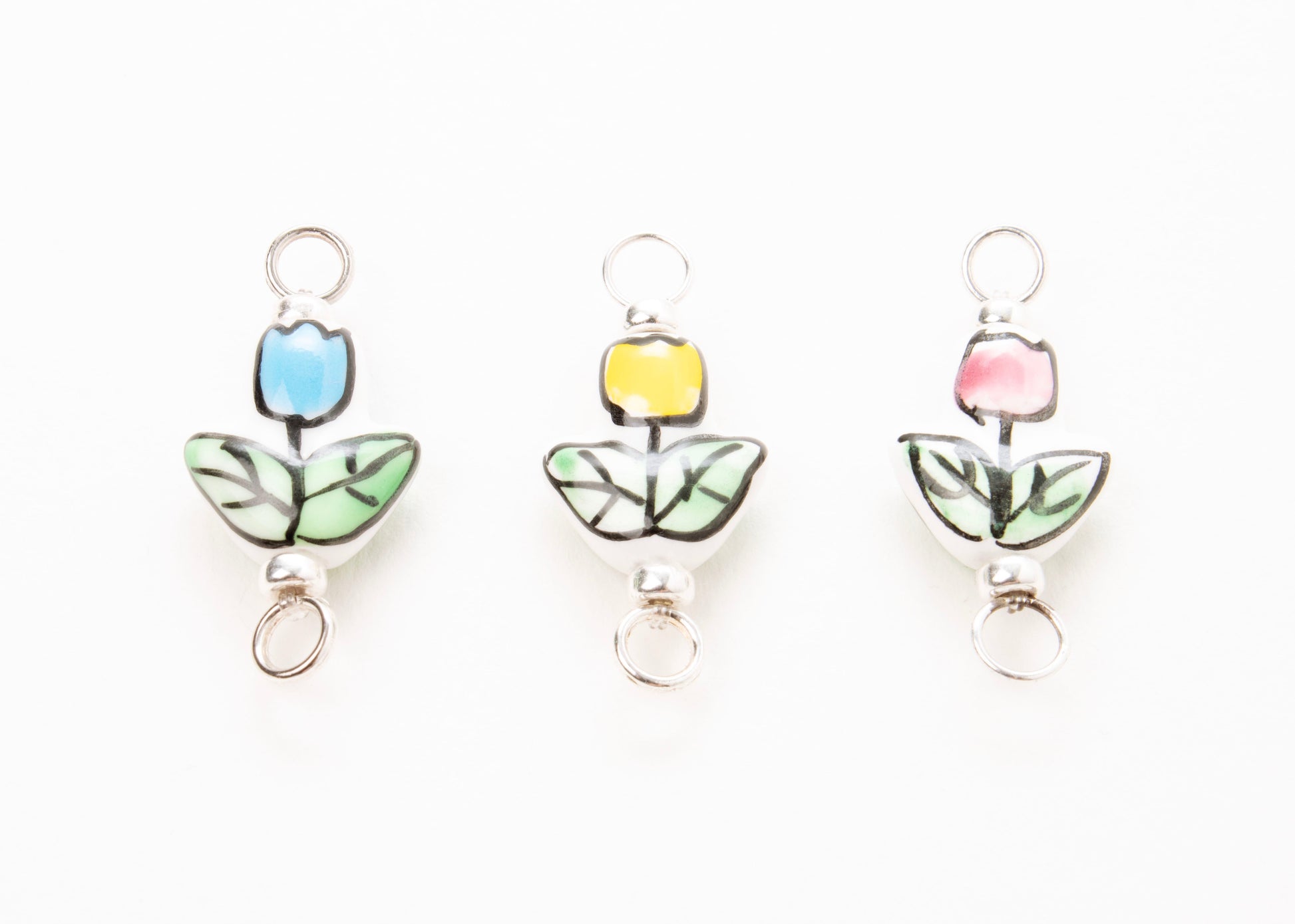 Front close up of  three hand painted tulip  porcelain_charms on light blue, yellow and pink_on a white background