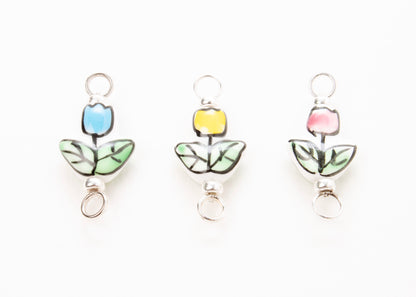 Front close up of  three hand painted tulip  porcelain_charms on light blue, yellow and pink_on a white background