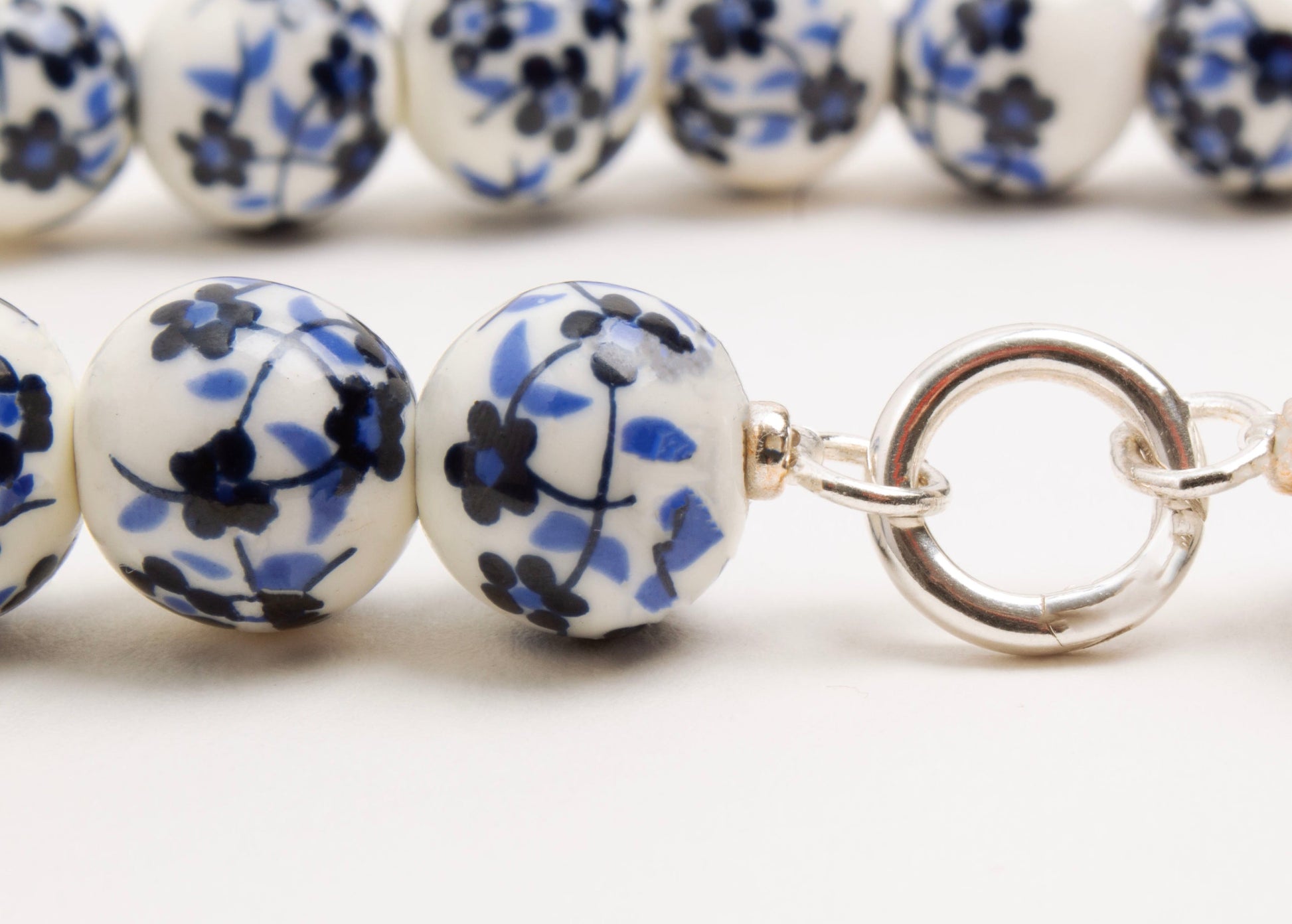 Close up of Sterling Silver looped endings of a white porcelain with blue hand painted flowers on a white background