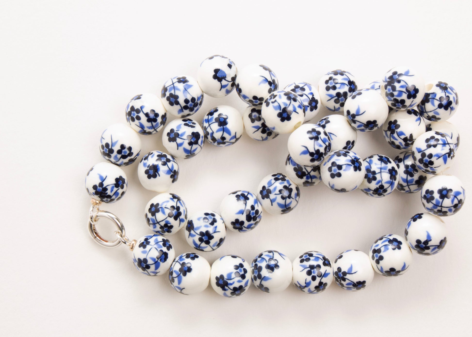 Plan view of a white porcelain with blue hand painted flowers and Sterling Silver looped endings on a white background