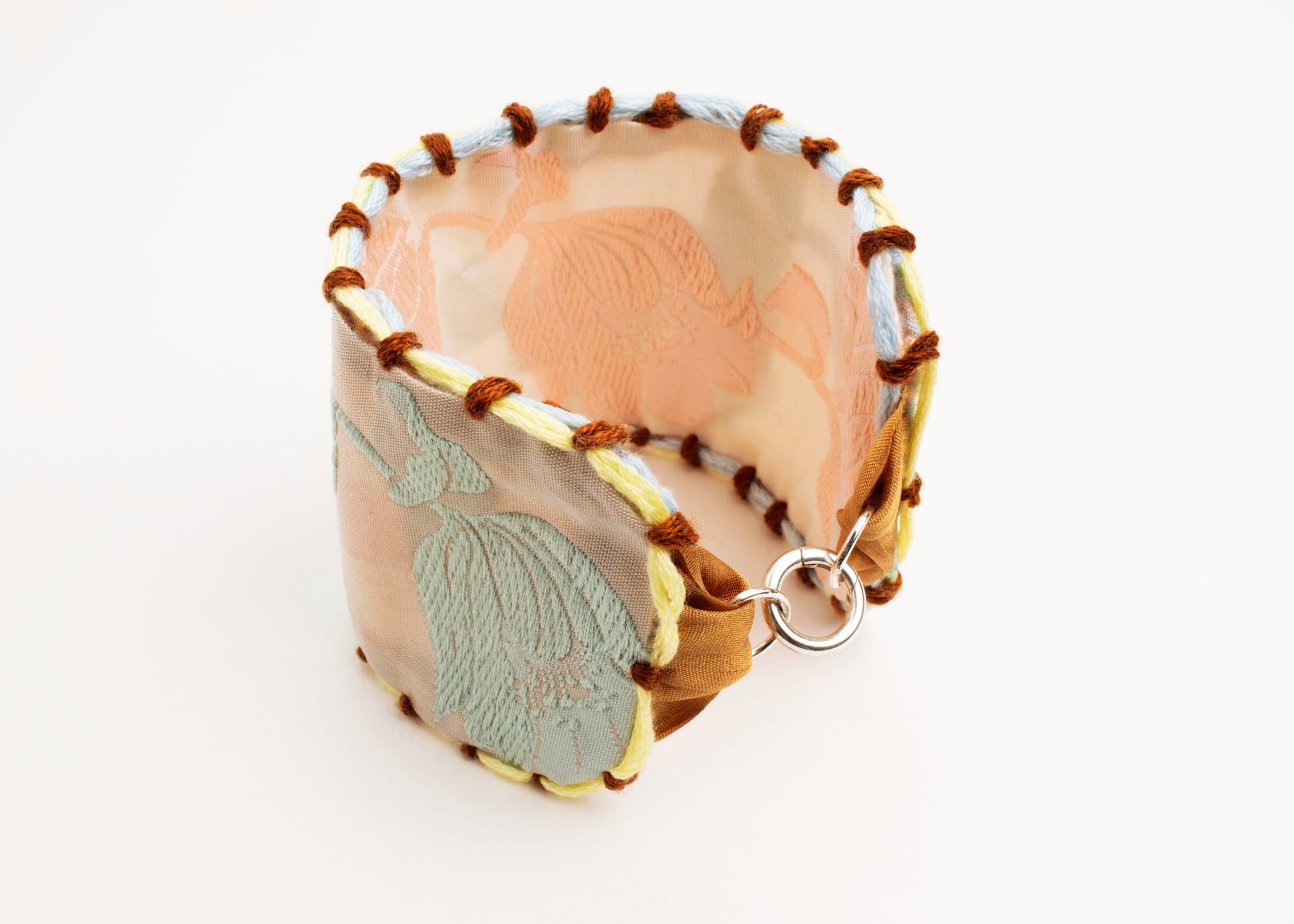 Front view of a closed reversible cotton woven strap bracelet with tulip motif in pink and light blue and pink and embroidered borders in brown, light blue and butter yellow and Sterling Silver looped endings detail on a white background.