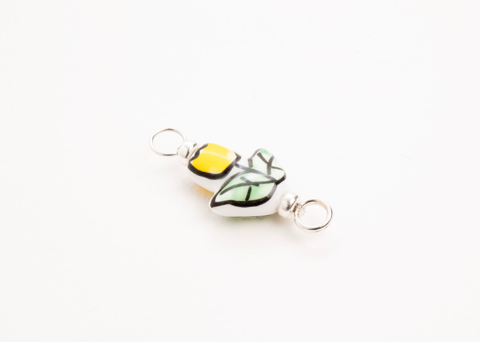 Side diagonal close up of a handprinted yellow_hand painted porcelain_tulip_charm_on a white background