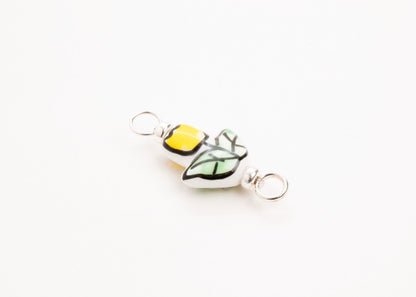 Side diagonal close up of a handprinted yellow_hand painted porcelain_tulip_charm_on a white background