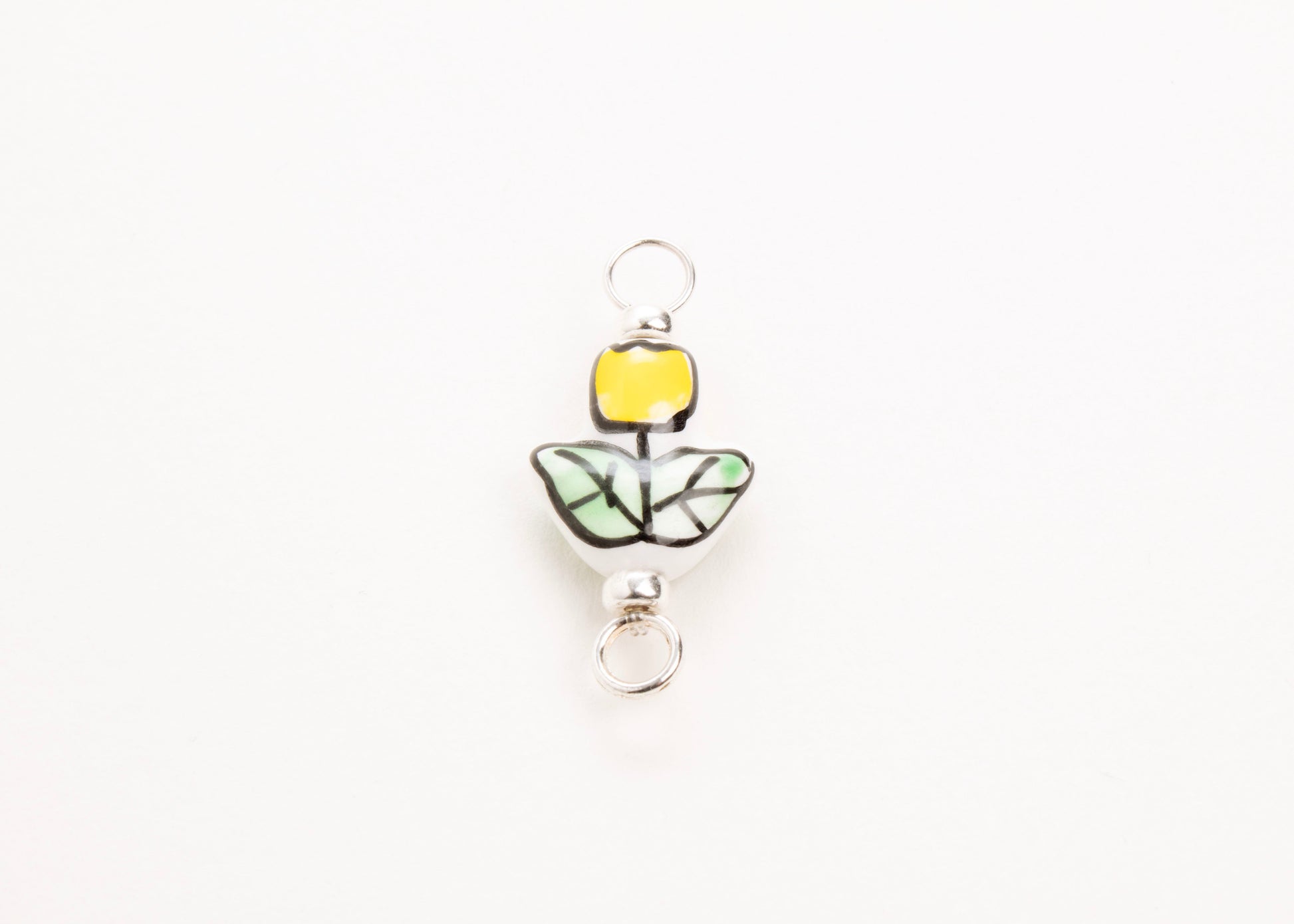 Front close up of a handprinted yellow_hand painted porcelain_tulip_charm_on a white background