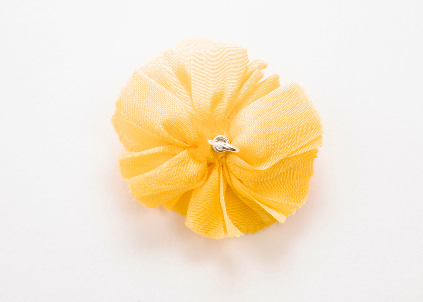 Back view of a yellow silk flower charm with sterling silver loop end on a white background.