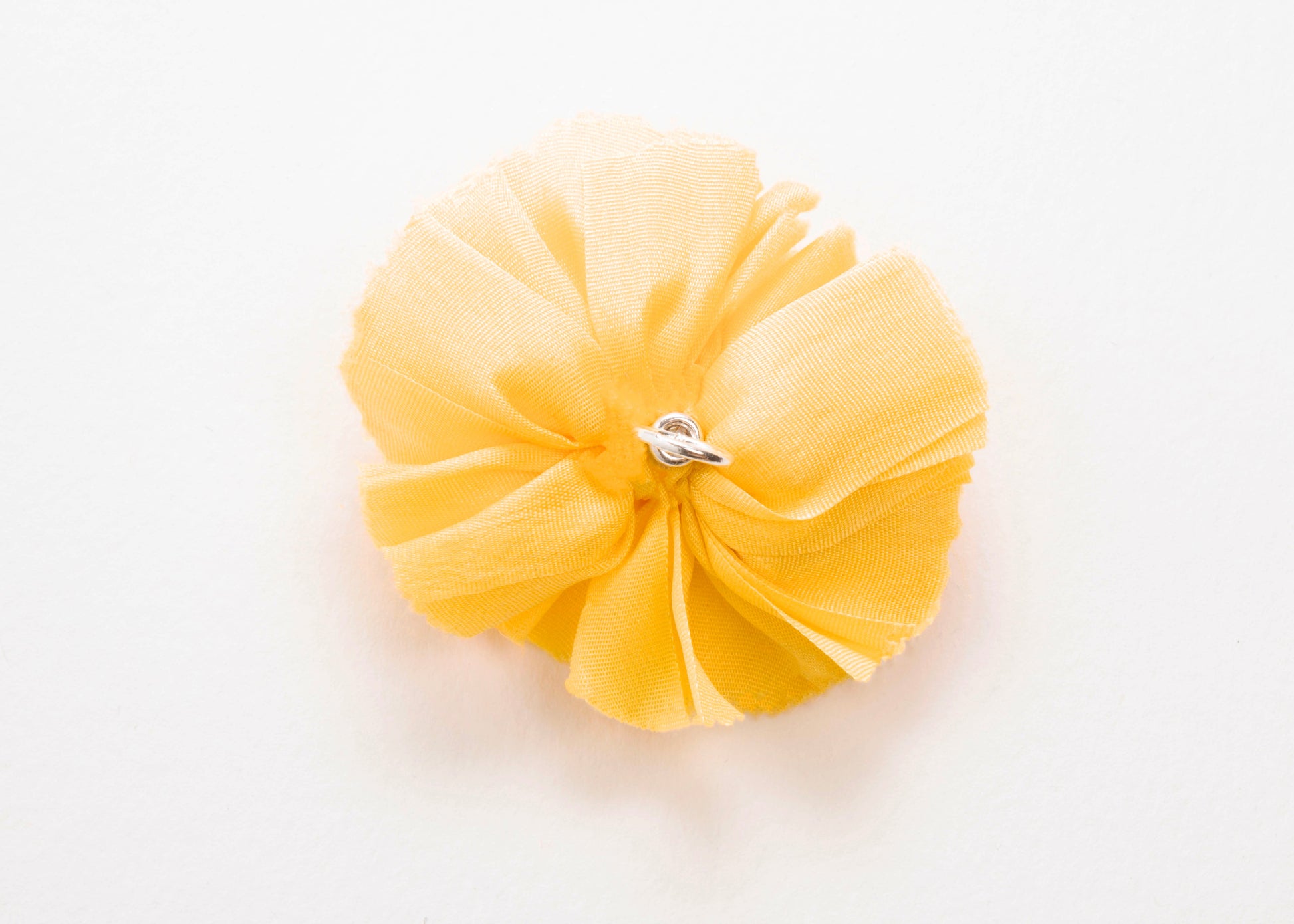 Back view of a yellow silk flower charm with sterling silver loop end on a white background.