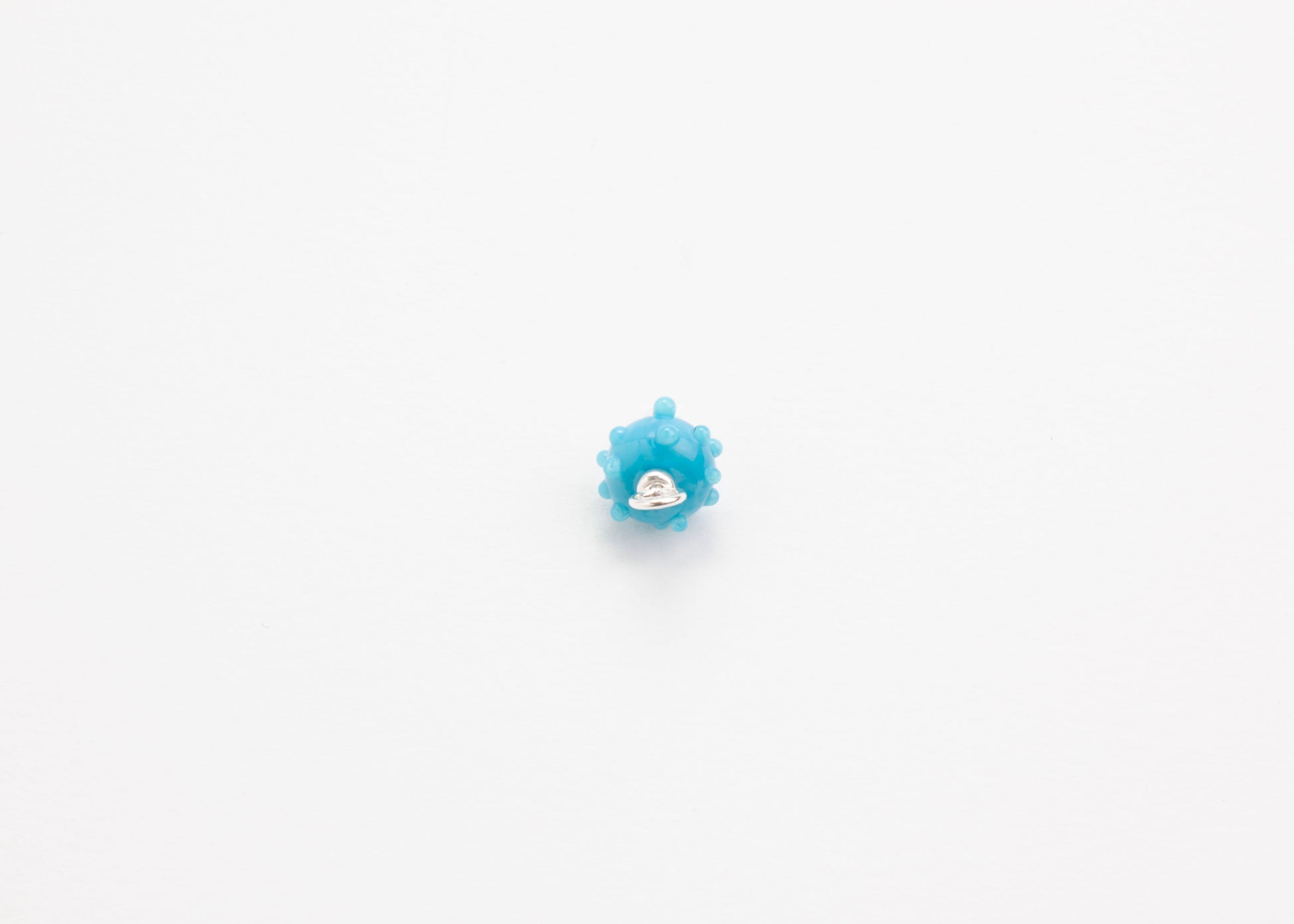 Front view of an urchin lampwork glass blue charm with Sterling Silver ends in a white background