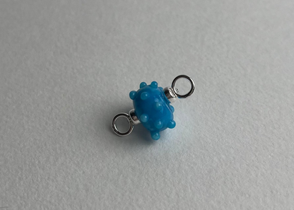 Close up of a blue urchin shaped bumpy lampwork charm with sterling silver ends on a white background