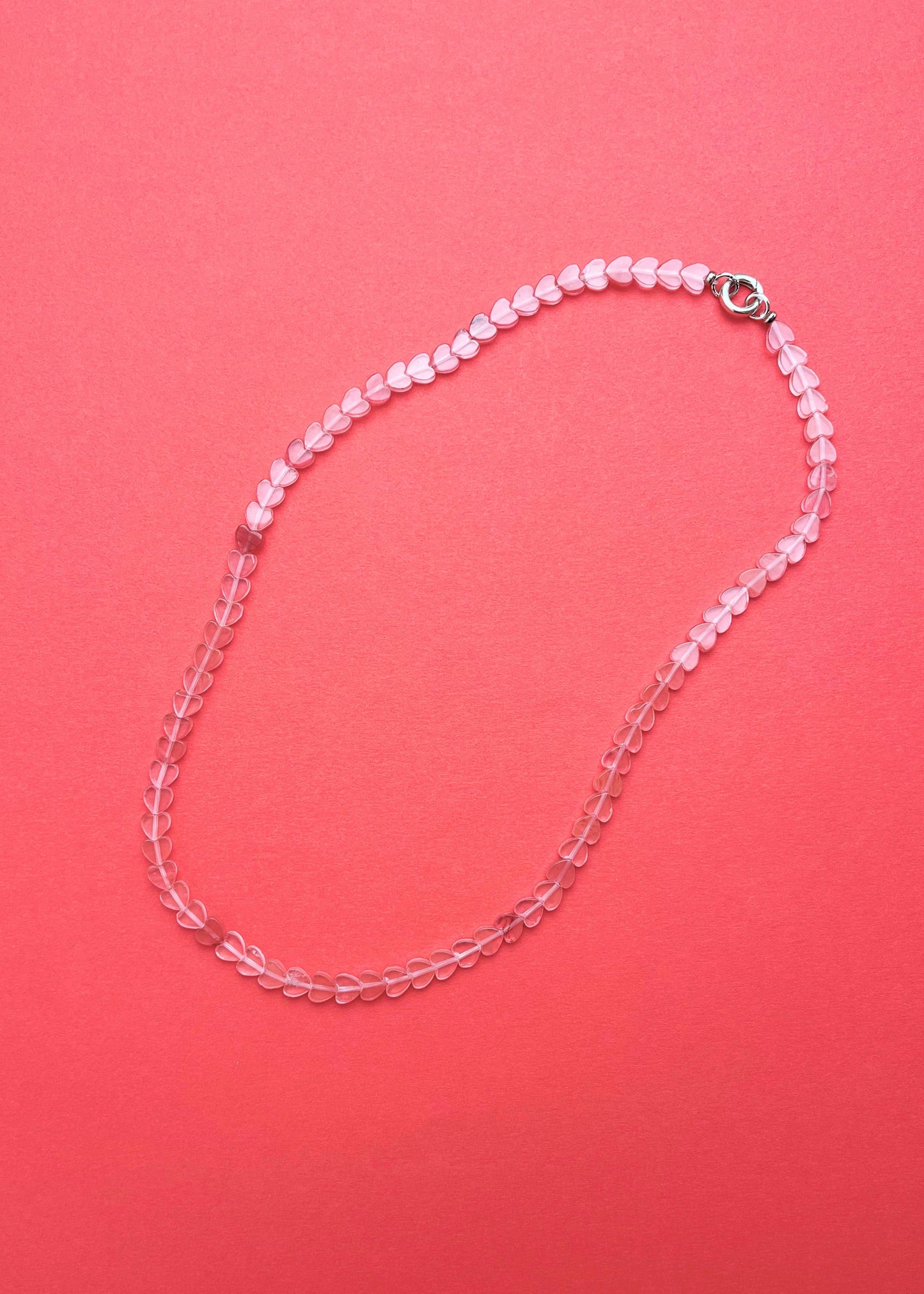 Overhead view of a cherry quartz heart shaped bead necklace with sterling silver endings on a pink-red background