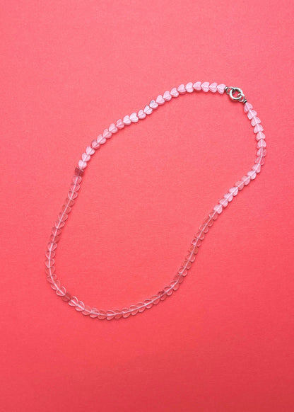Overhead view of a cherry quartz heart shaped bead necklace with sterling silver endings on a pink-red background