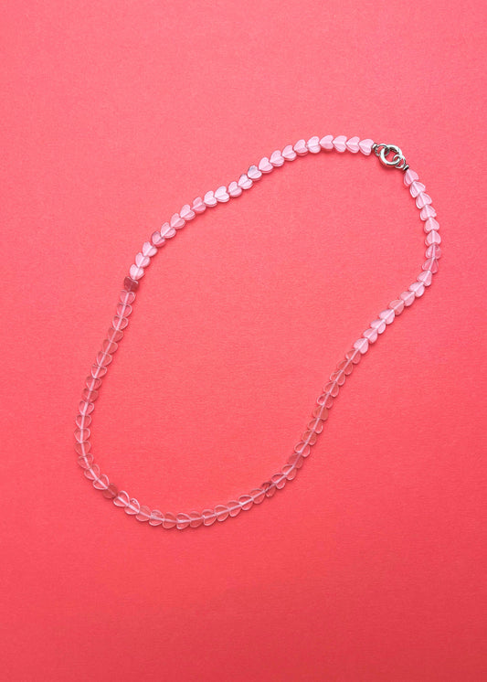 Overhead view of a cherry quartz heart shaped bead necklace with sterling silver endings on a pink-red background