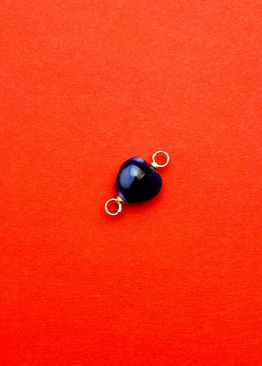 close up of a chunky blue porcelain heart charm with Sterling Silver endings on a red background