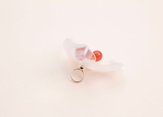 back side view of a clear white resin 3 petal flower charm with glass beads detail on a soft peach background