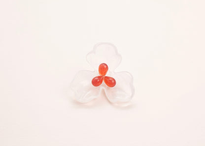 front view of a clear white resin 3 petal flower charm with glass beads detail on a soft peach background