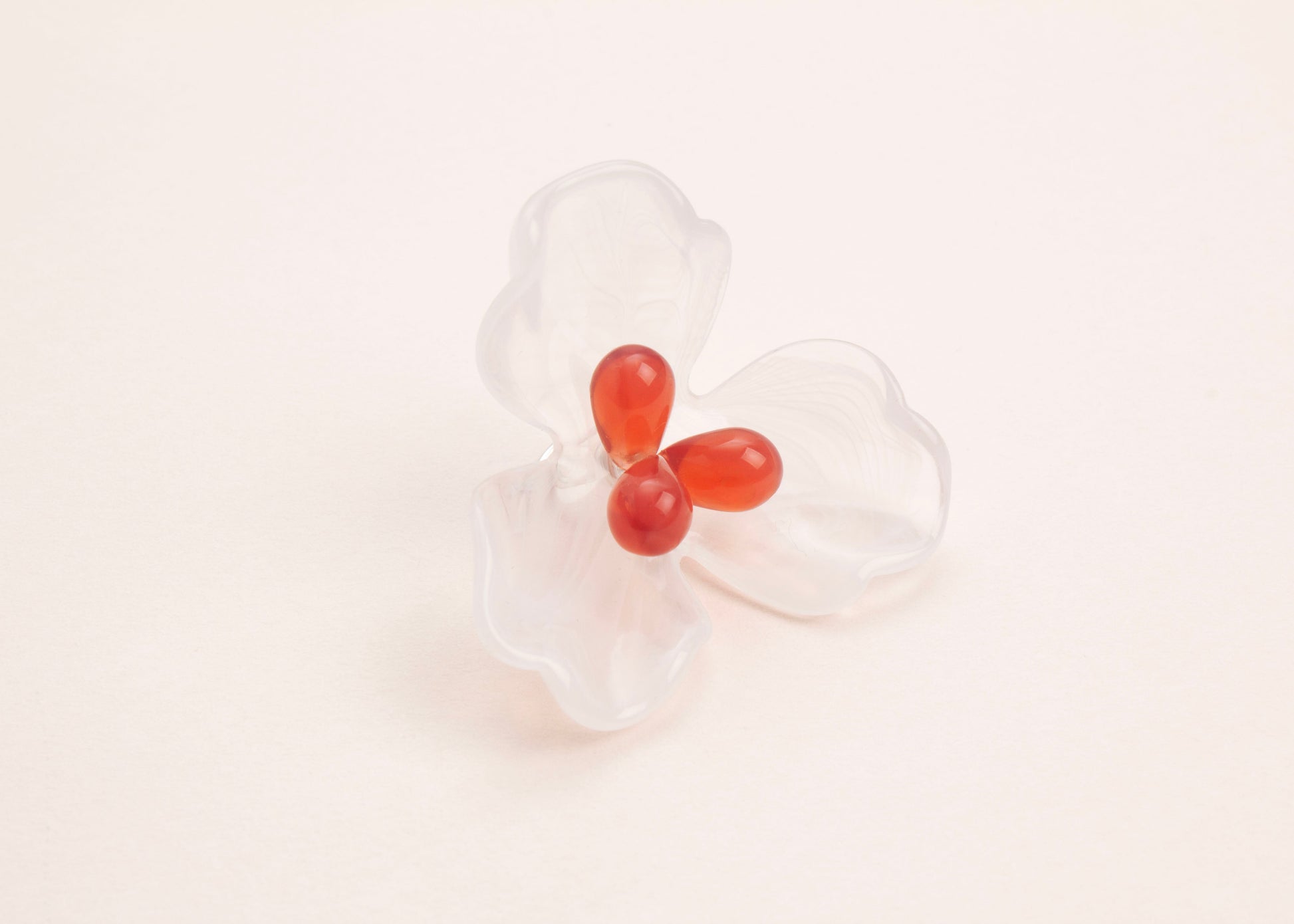 front side view of a clear white resin 3 petal flower charm with glass beads detail on a soft peach background