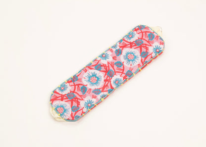 Plan view of a cotton woven reversible strap bracelet, with flower motifs and embroidered borders in persimmon and pink, teal and butter yellow with Sterling silver looped endings on a white background.