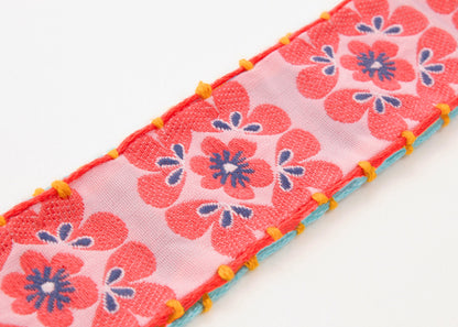 Close up of fabric detail of a cotton woven reversible strap bracelet, with squarish flower motifs in persimmon and pink and mellow yellow with Sterling silver looped endings on a white background.