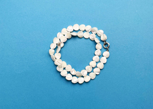 Overhead view of MOP heart shaped carved beads necklace strands placed in two loops over a sky blue background