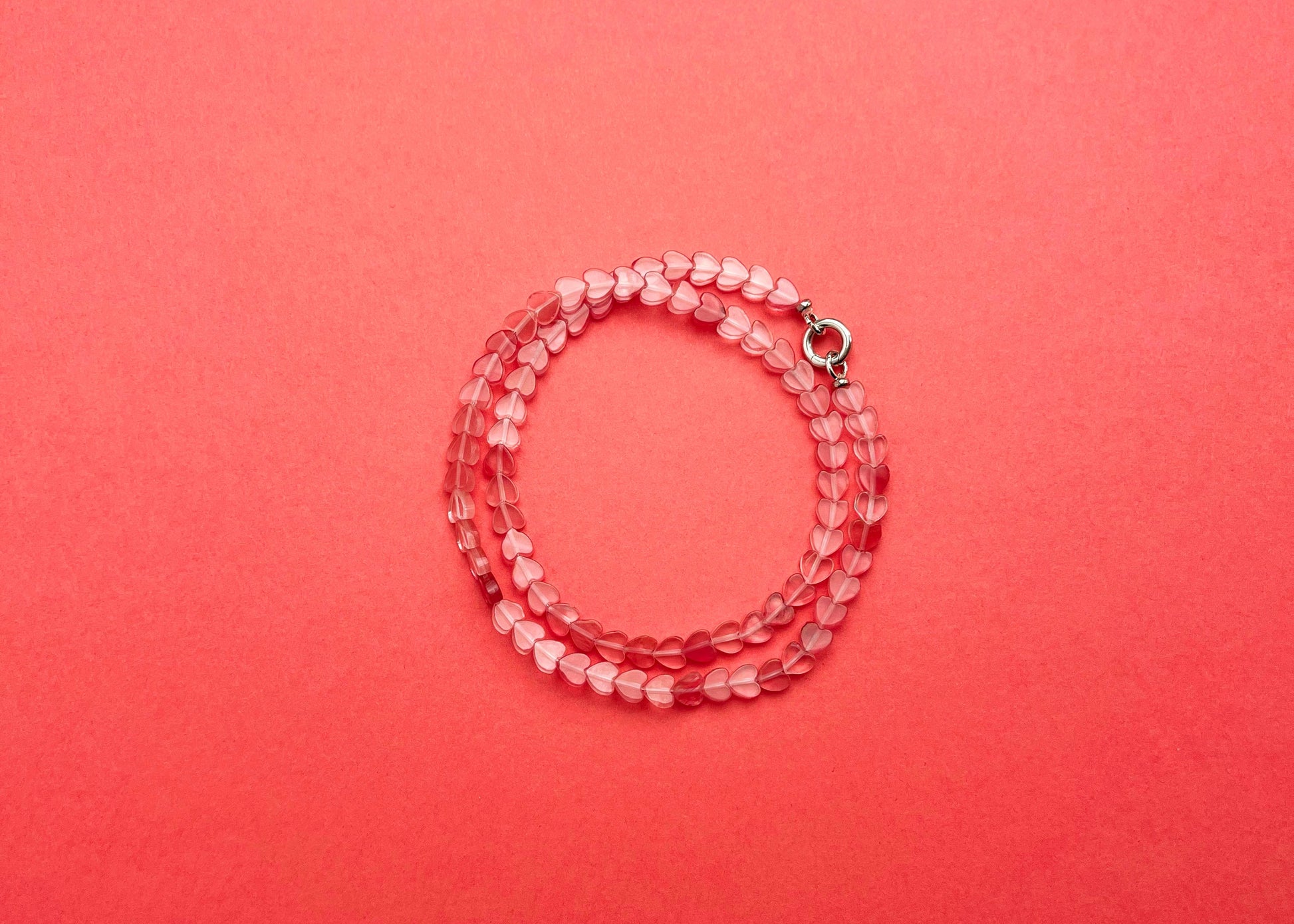 Overhead view of a cherry quartz heart shaped bead necklace with Sterling Silver endings placed on a double-loop on a pink-red background