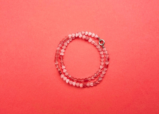 Overhead view of a cherry quartz heart shaped bead necklace with Sterling Silver endings placed on a double-loop on a pink-red background