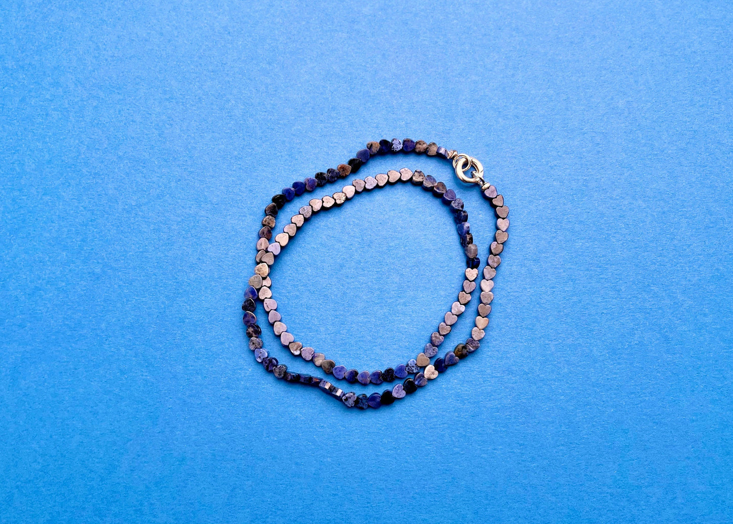 Overhead view of a lapislazuli heart shaped carved beads necklace with Sterling Silver endings placed in two loops on a navy blue background