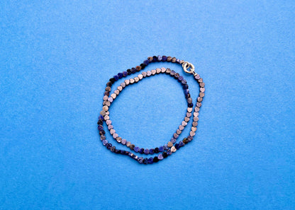 Overhead view of a lapislazuli heart shaped carved beads necklace with Sterling Silver endings placed in two loops on a navy blue background