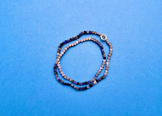 Overhead view of a lapislazuli heart shaped carved beads necklace with Sterling Silver endings placed in two loops on a navy blue background
