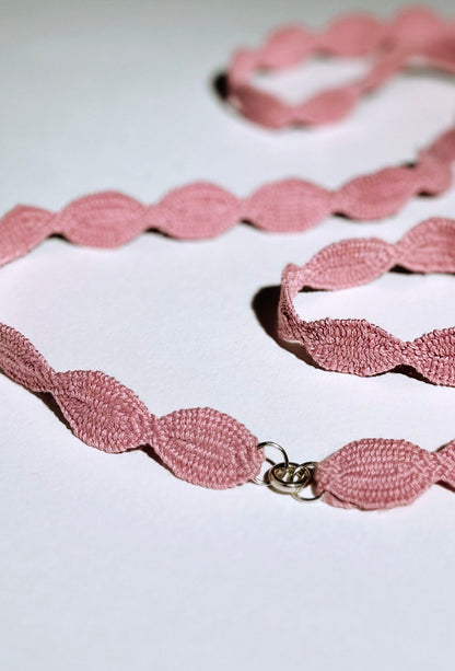Close view at the fabric and endings detail of a pink cotton interwoven ovals necklace with Sterling Silver endings placed in a double loop on a white background