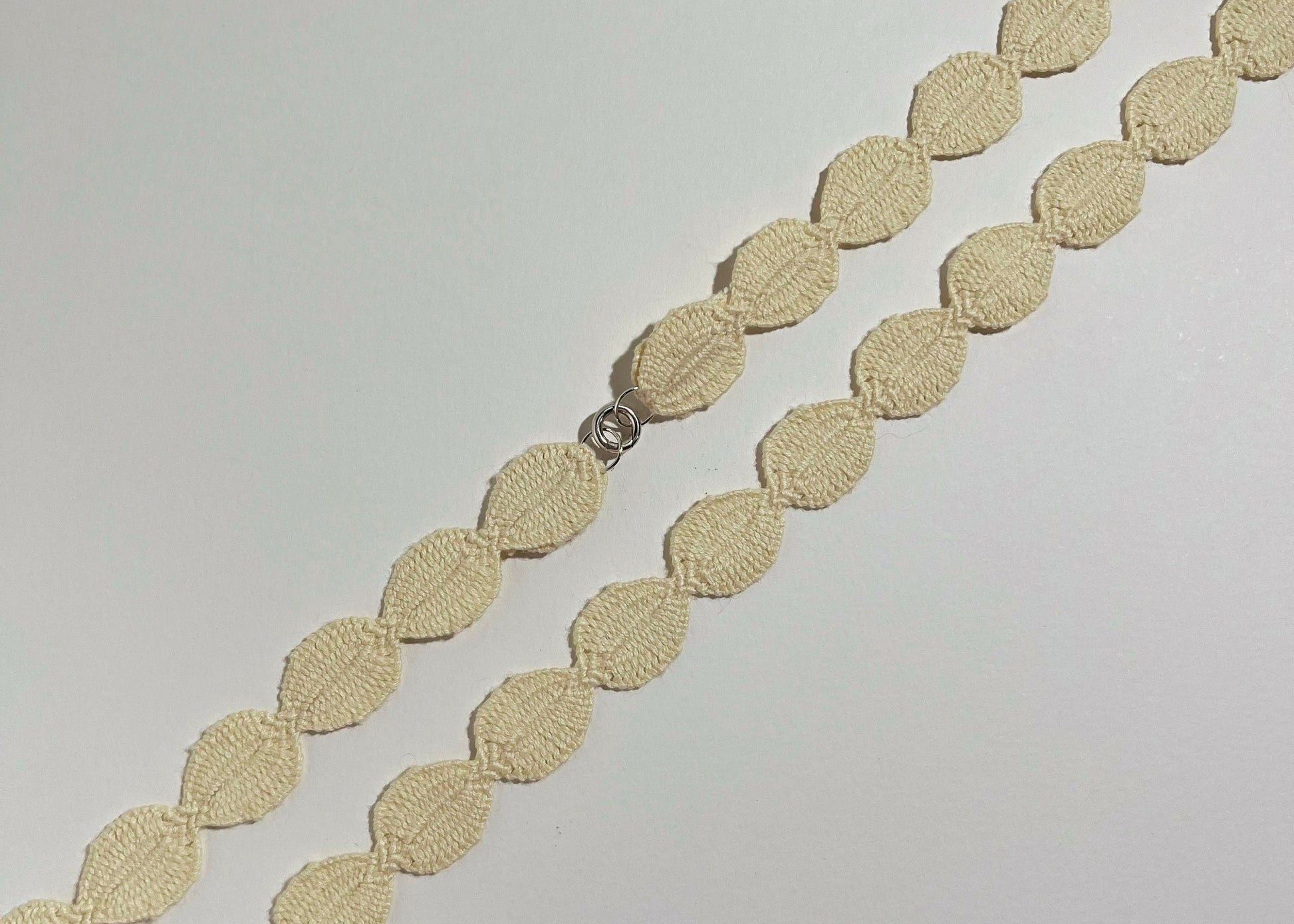 Overhead close look of an ivory cotton woven ovals necklace with Sterling Silver endings placed in diagonally on an ivory background