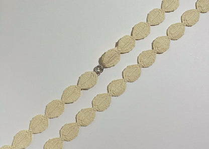 Overhead close look of an ivory cotton woven ovals necklace with Sterling Silver endings placed in diagonally on an ivory background