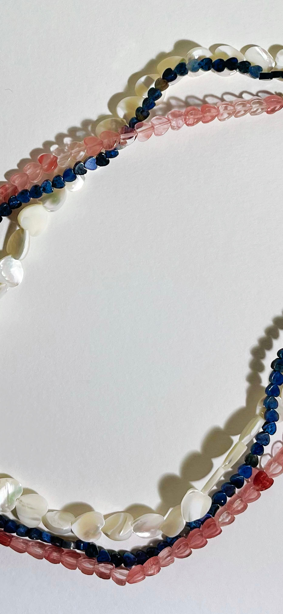 Close up detail of the stands of a Cherry Quartz, MOP and Lapis Lazuli gemstone heart shaped beaded necklaces on a white background 
