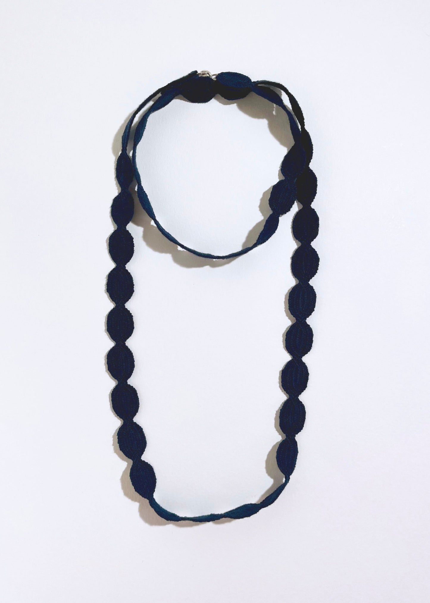 Overhead view of a navy cotton woven ovals necklace with Sterling Silver endings placed in double loop chocker with long drop on a white background
