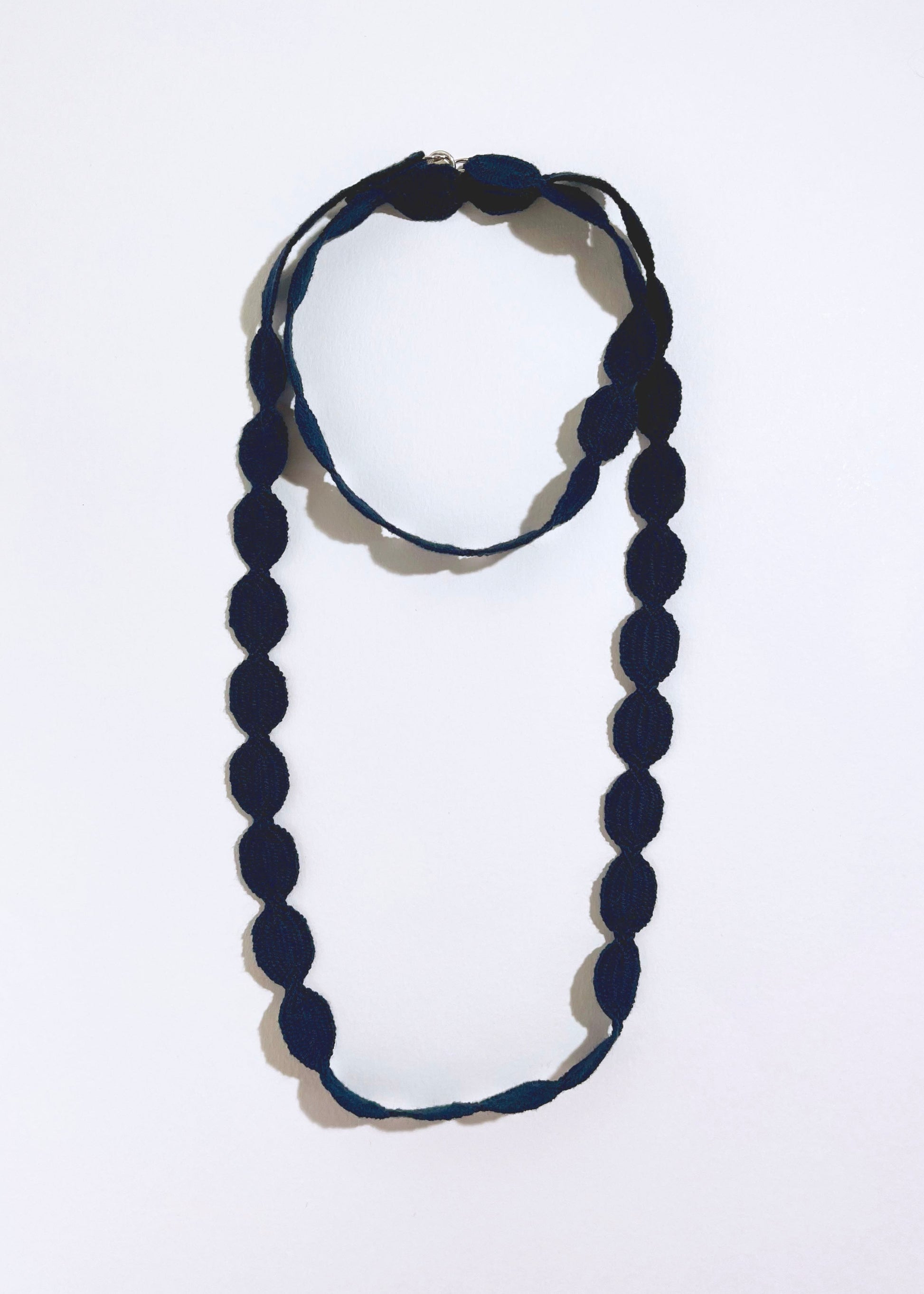 Overhead view of a navy cotton woven ovals necklace with Sterling Silver endings placed in double loop chocker with long drop on a white background