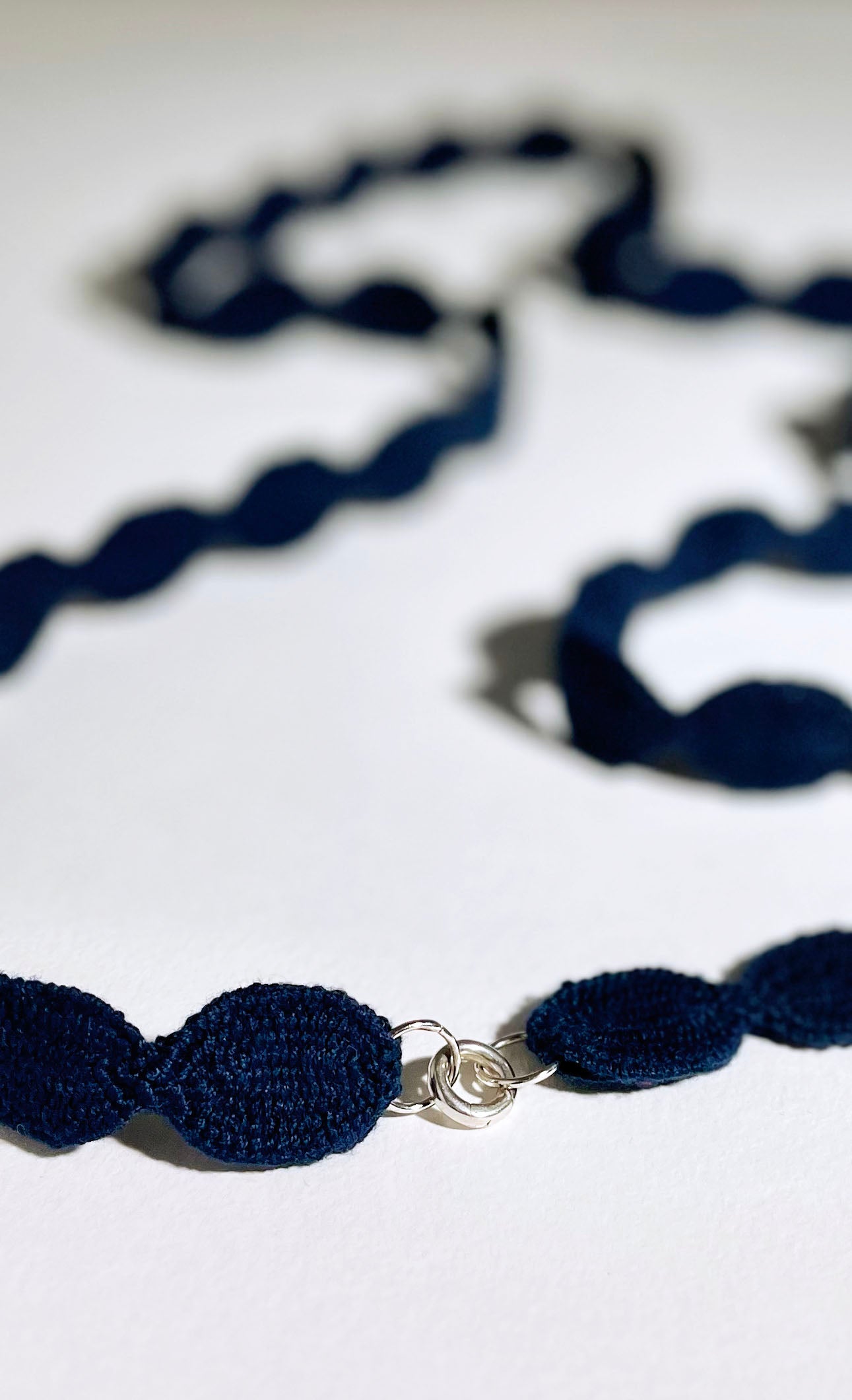 Close view of the Sterling Silver endings of an interwoven cotton ovals necklace in navy blue laid on a white background.