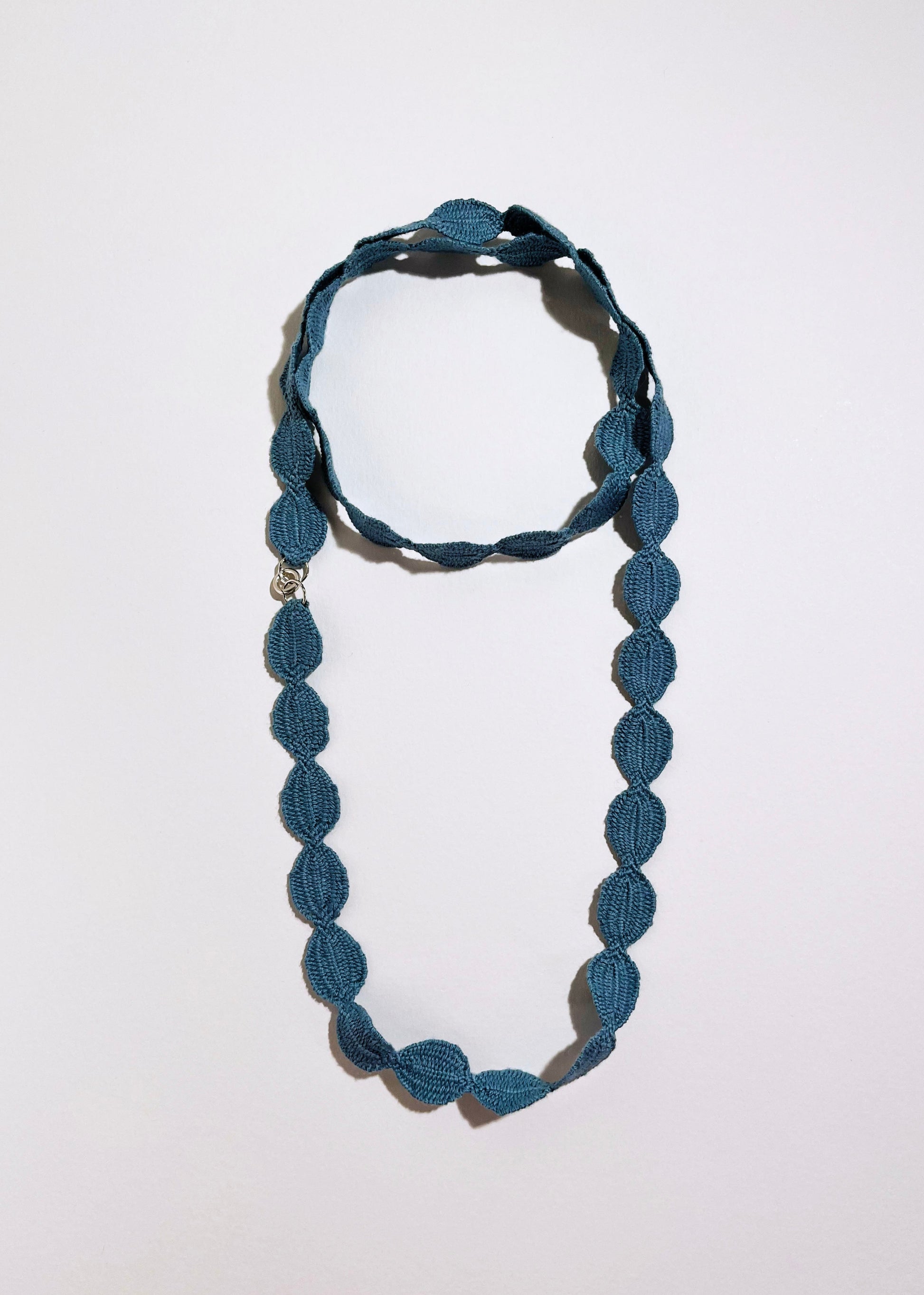 Overhead view of sky blue cotton woven ovals necklace with Sterling Silver endings placed in double loop chocker with long drop on a white background