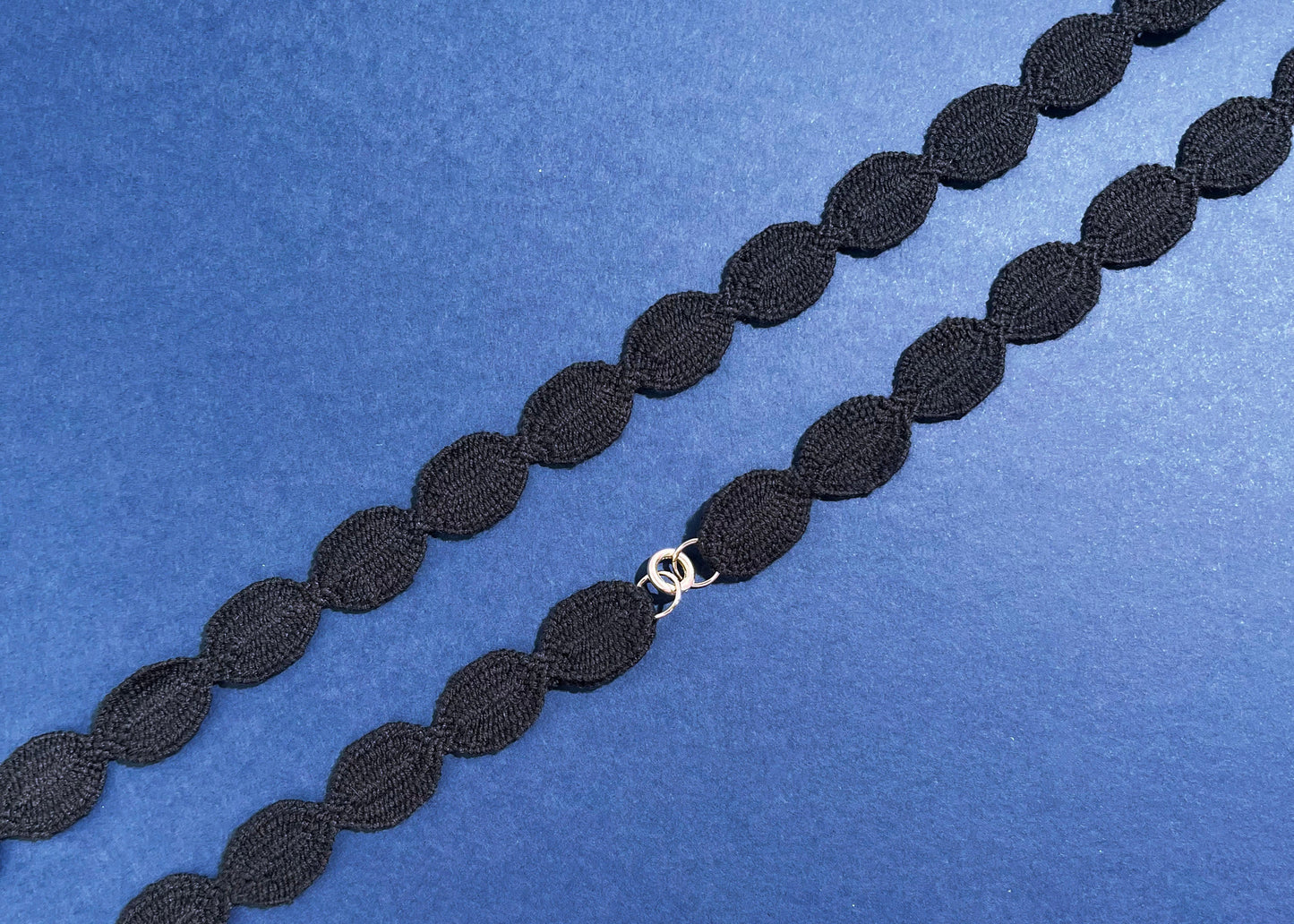 Overhead close look at a navy cotton woven ovals necklace with Sterling Silver endings placed in diagonally on a navy background