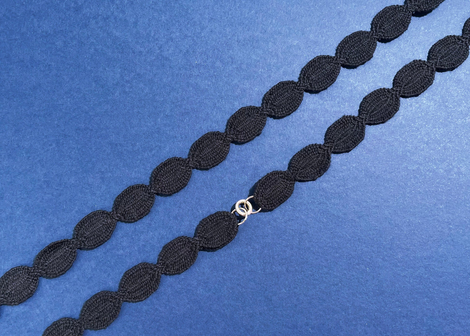 Overhead close look at a navy cotton woven ovals necklace with Sterling Silver endings placed in diagonally on a navy background