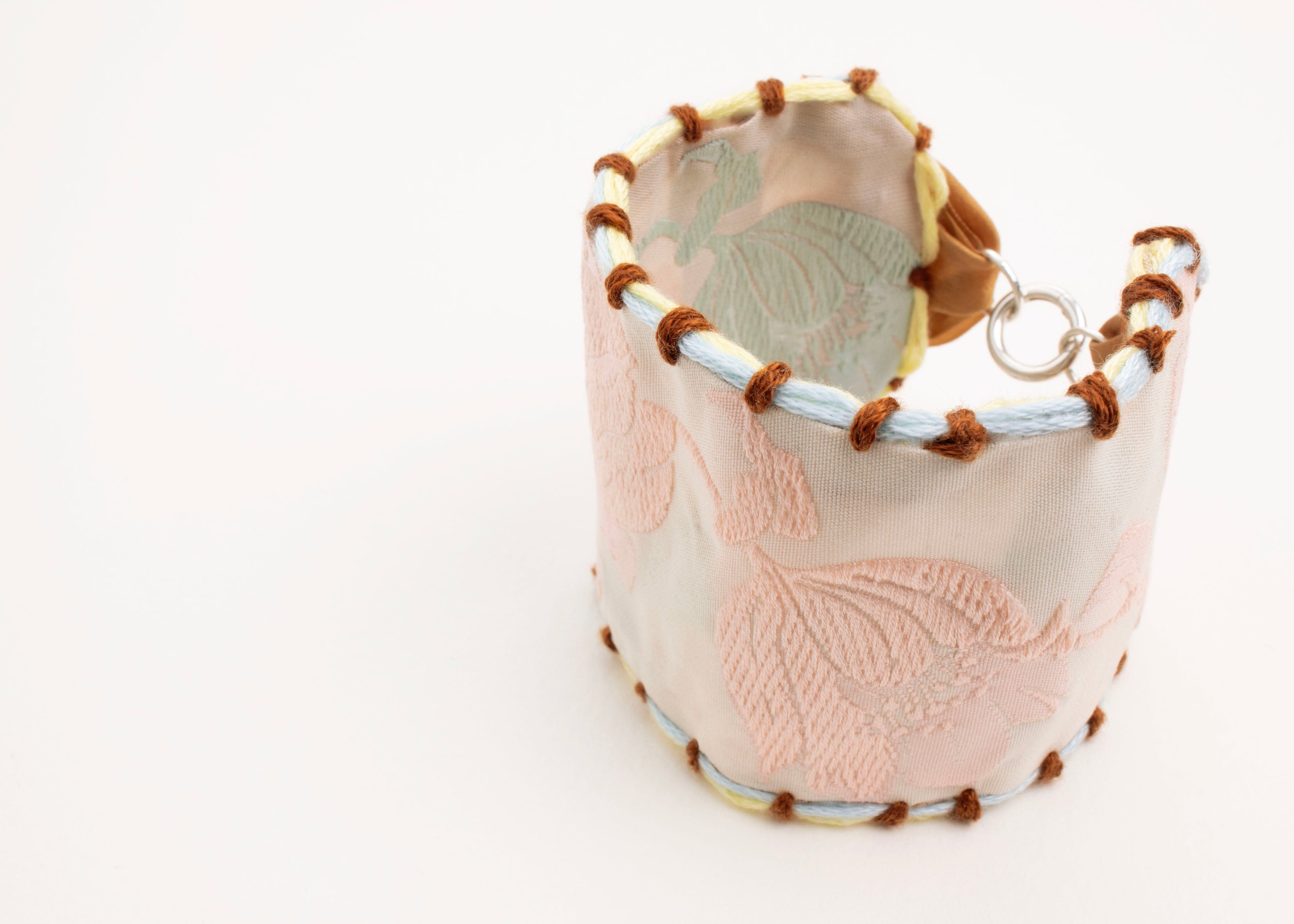 Back view of a reversible cotton woven strap bracelet with tulip motif in pink and light blue and embroidered borders in brown, light blue and butter yellow with Sterling Silver looped endings detail on a white background.
