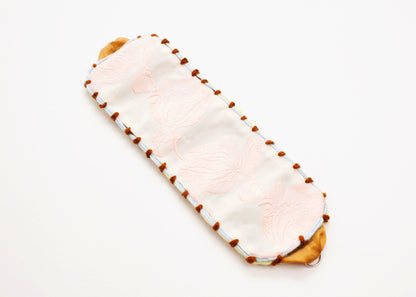 Diagonal plan view of an open reversible cotton woven strap bracelet with tulip motif in pink and embroidered borders in brown and light blue with Sterling Silver looped endings detail on a white background.