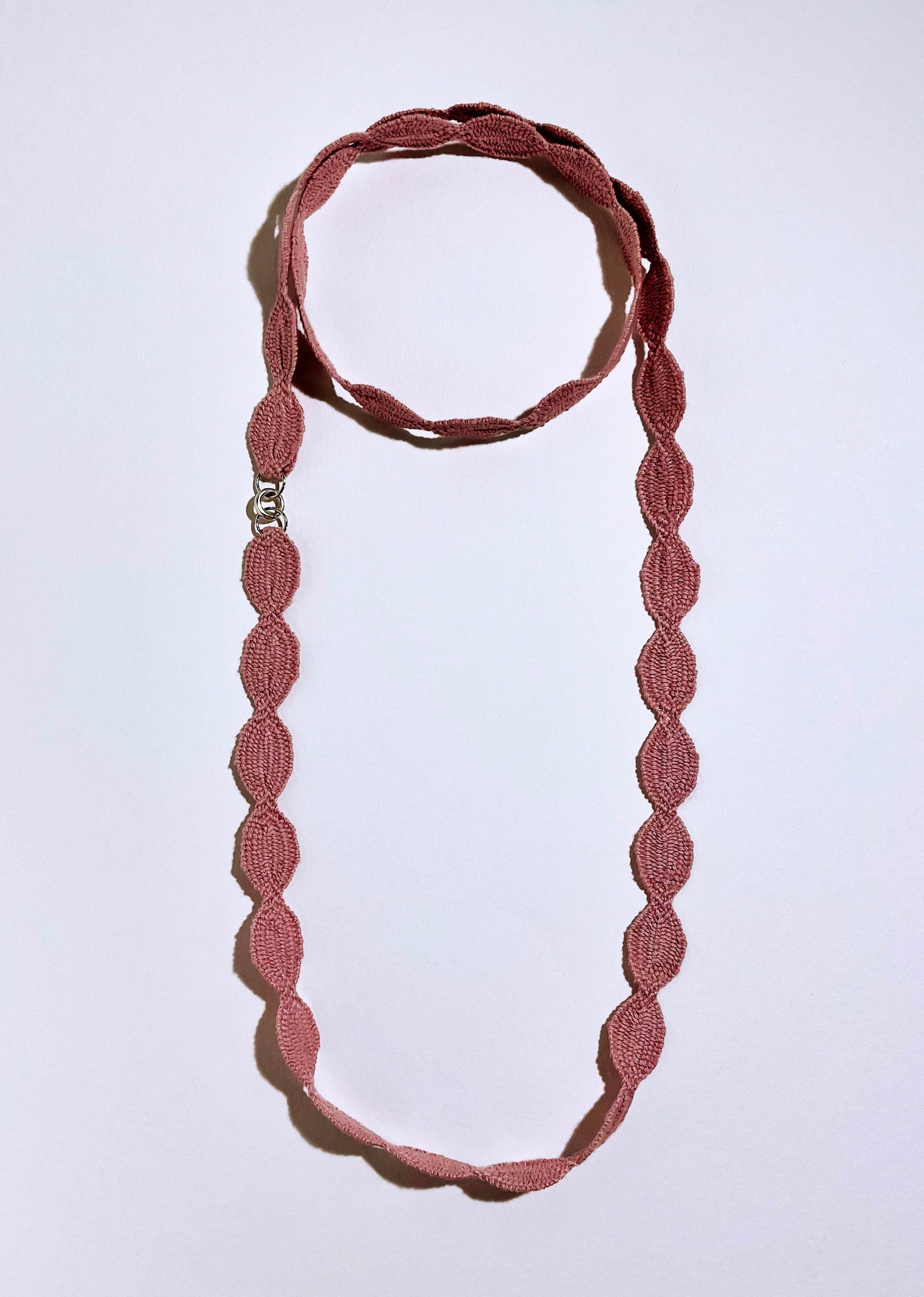 Overhead view of a pink cotton interwoven ovals necklace with Sterling Silver endings placed in a double loop as a choker with long drop on a white background