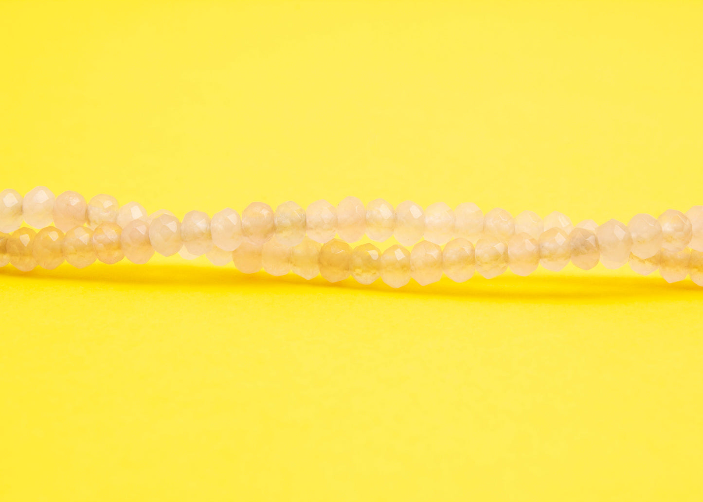 Front view beads detail of a pink quartzite beaded necklace with Sterling Silver looped endings on a yellow background