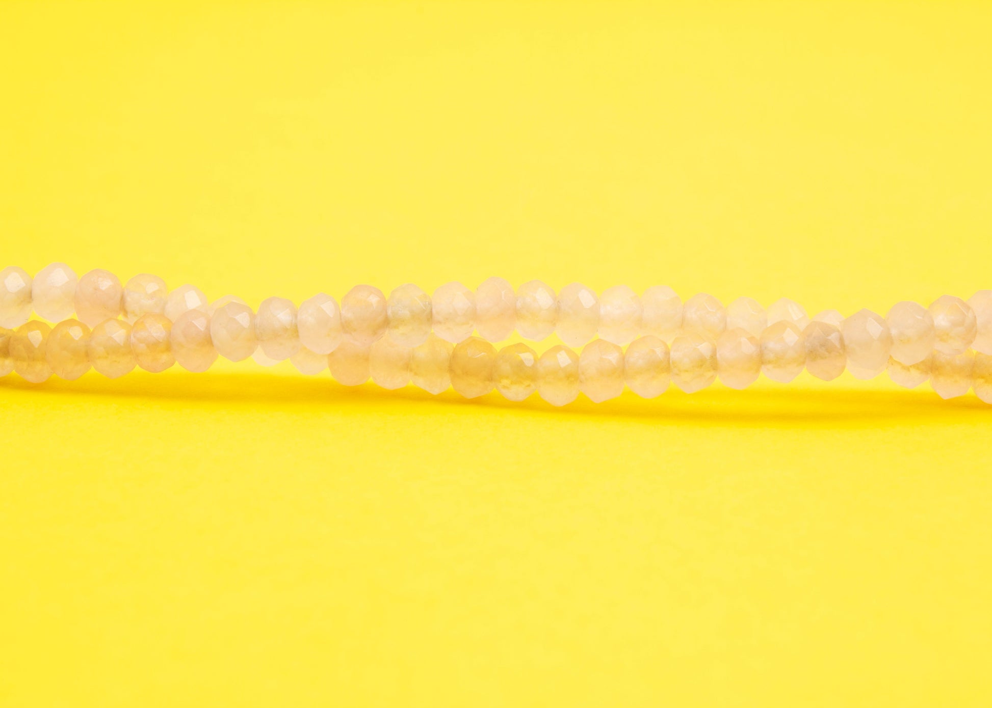 Front view beads detail of a pink quartzite beaded necklace with Sterling Silver looped endings on a yellow background