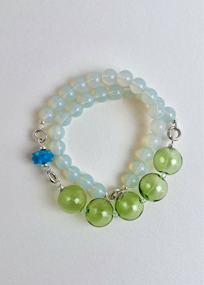 Overhead view of a ready to wear necklace made with green blue Opalite chainlets, green chunky glass bead drop and a cerulean bumpy glass charm with Sterling Silver endings on a white background