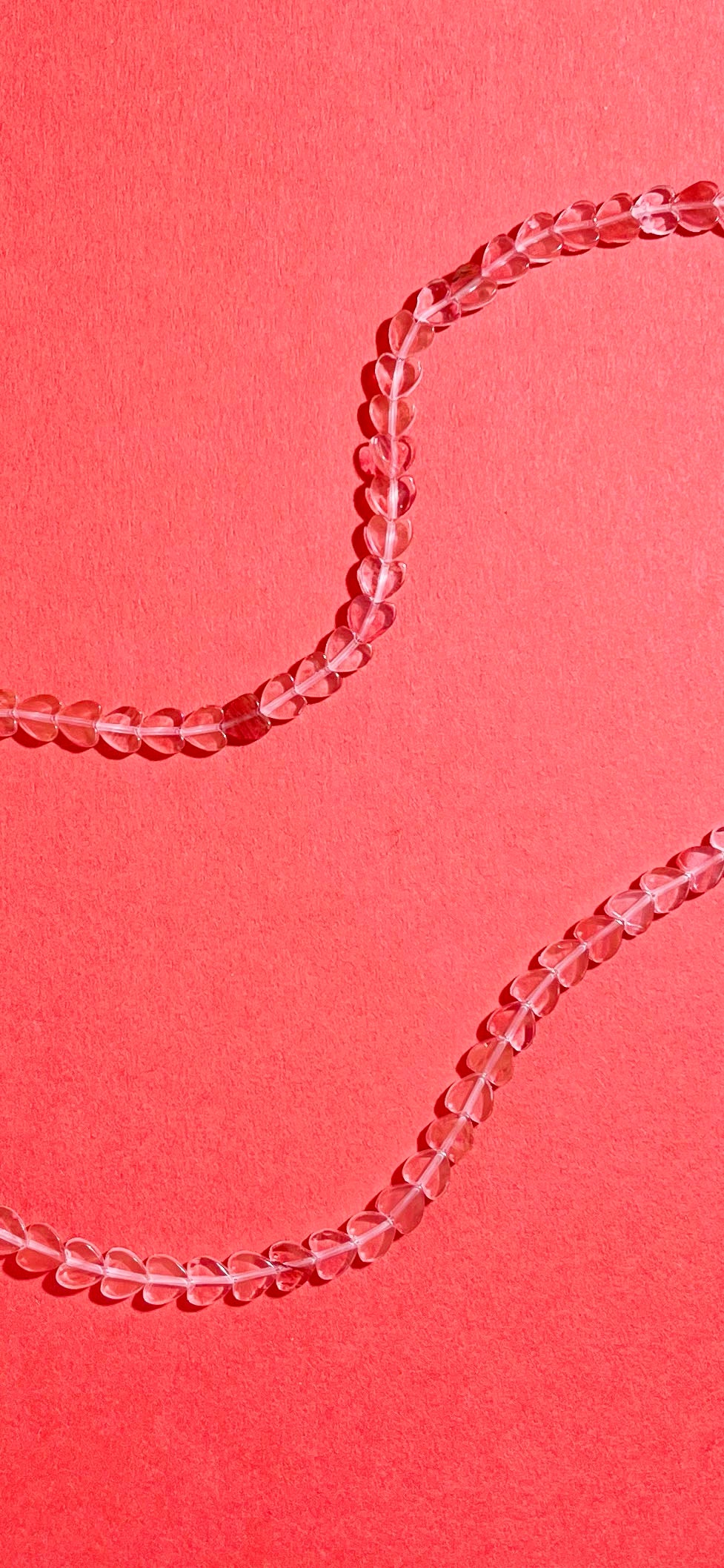 Closer look of the strands of a cherry quartz heart-shaped beads necklace with Sterling Silver endings on a pink-red background