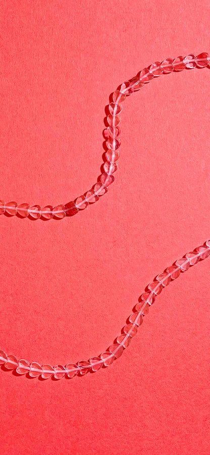 Closer look of the strands of a cherry quartz heart-shaped beads necklace with Sterling Silver endings on a pink-red background