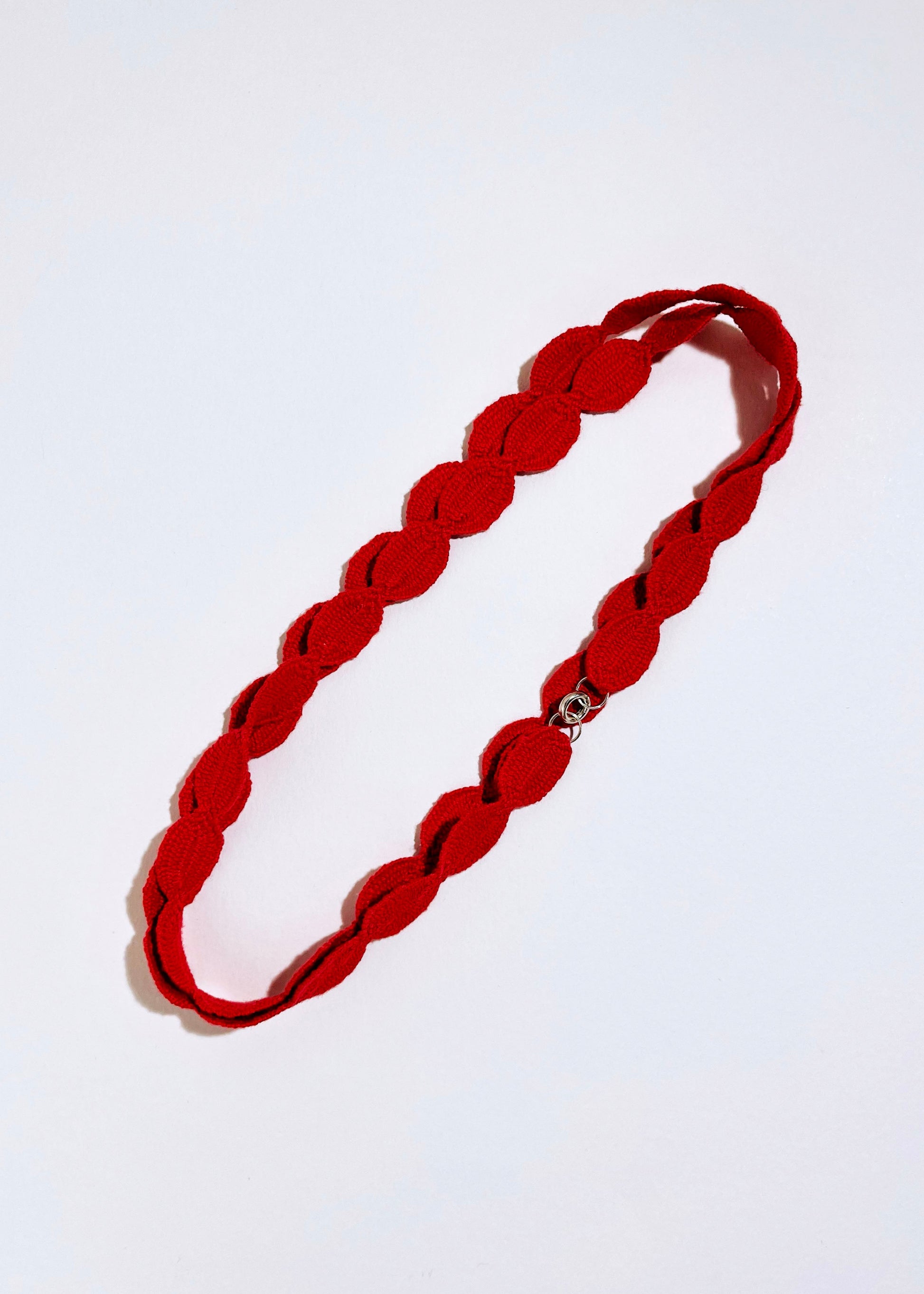 Overhead view of a red interwoven cotton ovals necklace with Sterling Silver endings placed in double loop diagonally on a white background