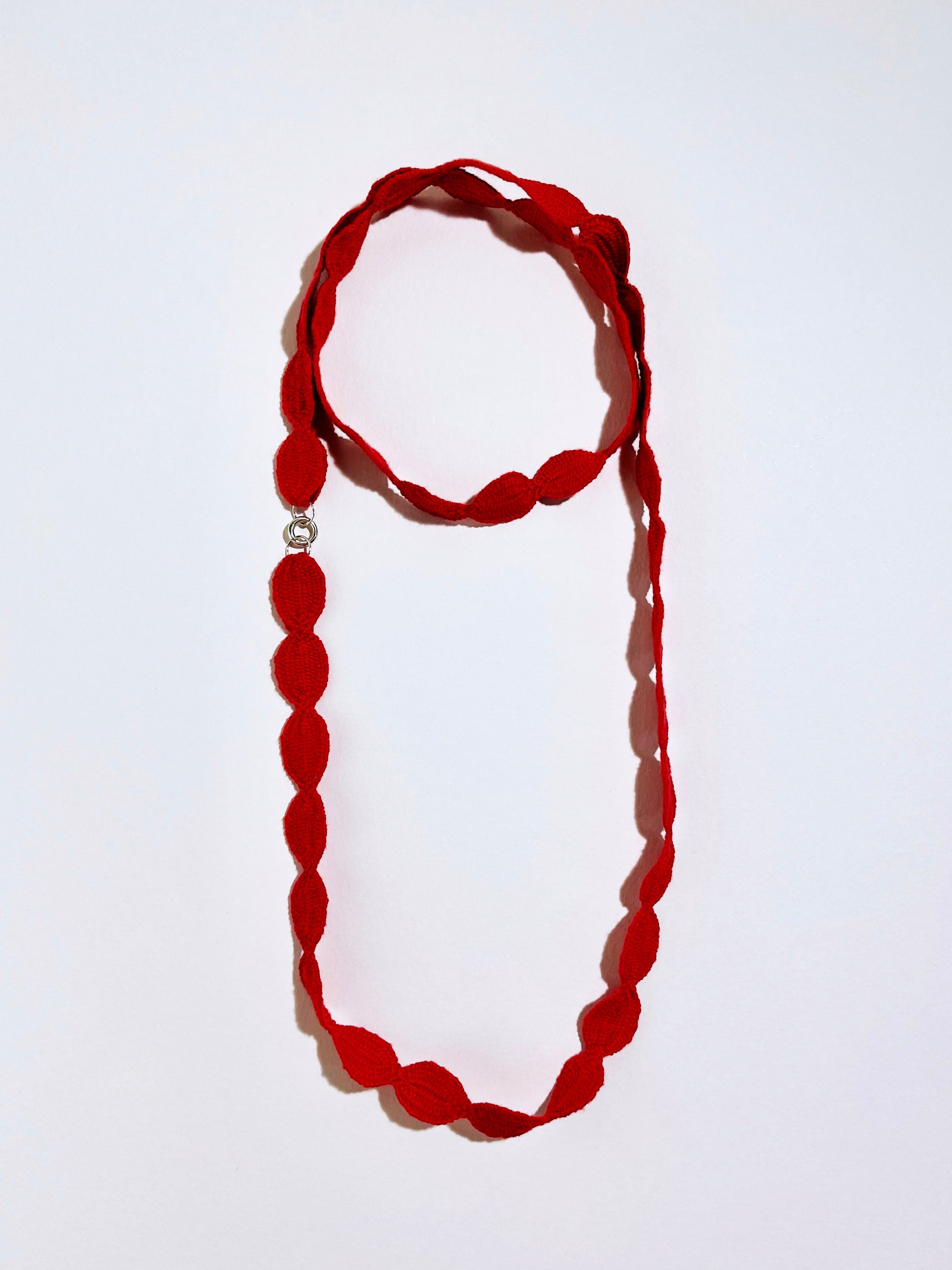Overhead view of a red interwoven cotton ovals necklace with Sterling Silver endings double looped into a chocker with long drop on a white background 